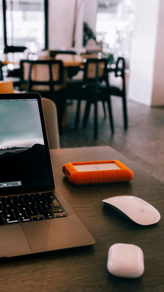 A cozy indoor workspace featuring a laptop, hard drive, mouse, and earphones.