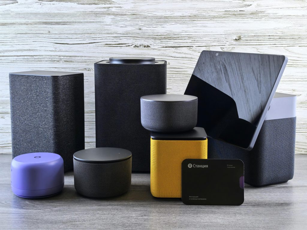 A collection of various smart home speakers and tablet displayed on a wooden surface.