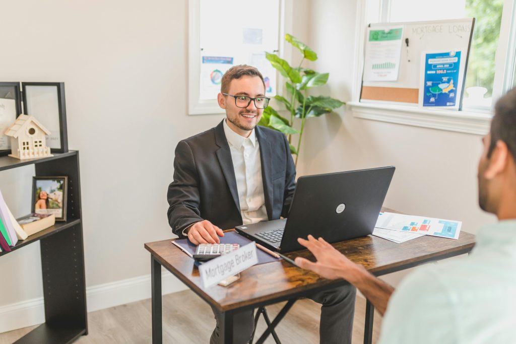 Mortgage broker in an office meeting with a client, utilizing a laptop.