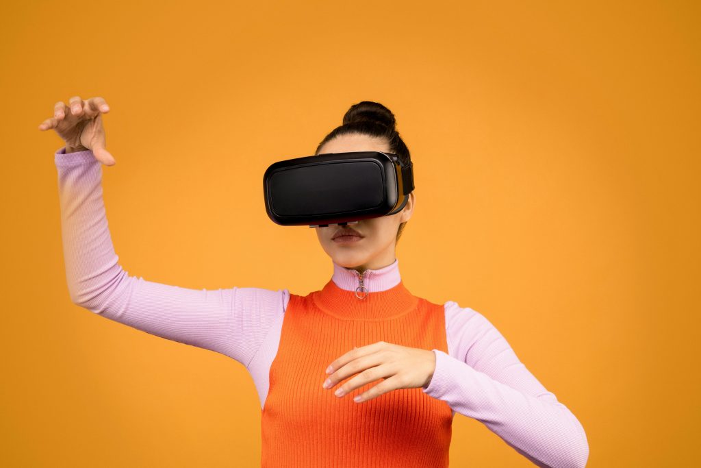 Woman using a VR headset with gestures against a bright orange background, showcasing immersion.